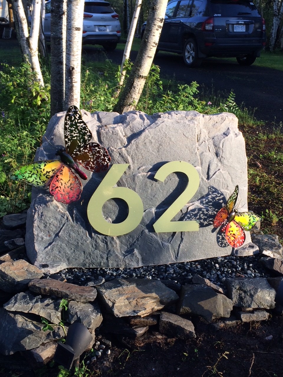 A photo of a faux rock with butterflies and address displayed on it.