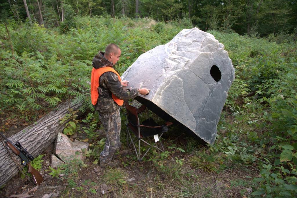 A hunter moving a fake rock to make it his camoflauge