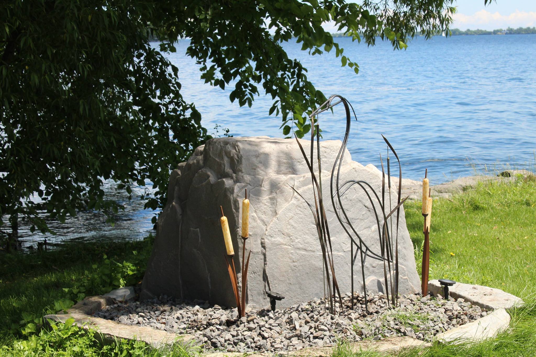 Large fake rock being used in a landscape by a lake.