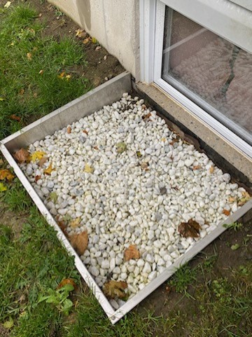 A photo of a square window well filled with gravel
